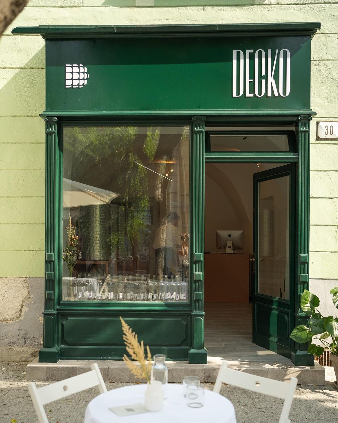 Zelená fasáda vinárky Decko s otvorenými dverami a bielym stolíkom pred vchodom.