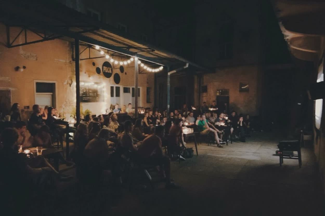 Letné kino vo dvore, ľudia sedia pri sviečkach pod svetielkami.