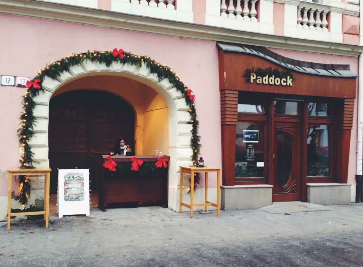 Vianočne vyzdobená brána domu číslo 17 na Mierovom námestí, v nej starý drevený bar s červenými mašľami, vedľa výklad Paddocku.