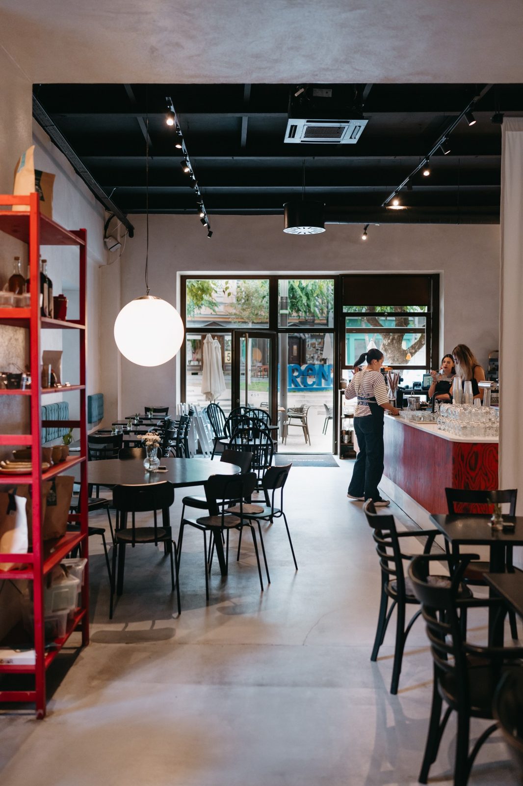 Interiér Paddocku: červený bar, čierne stoly a stoličky, veľká guľatá lampa a výhľad cez presklený vchod na námestie.