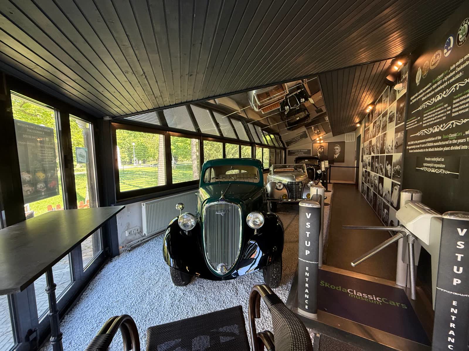 Presklená hala s historickými autami Škoda a turniketom pri vstupe do múzea.